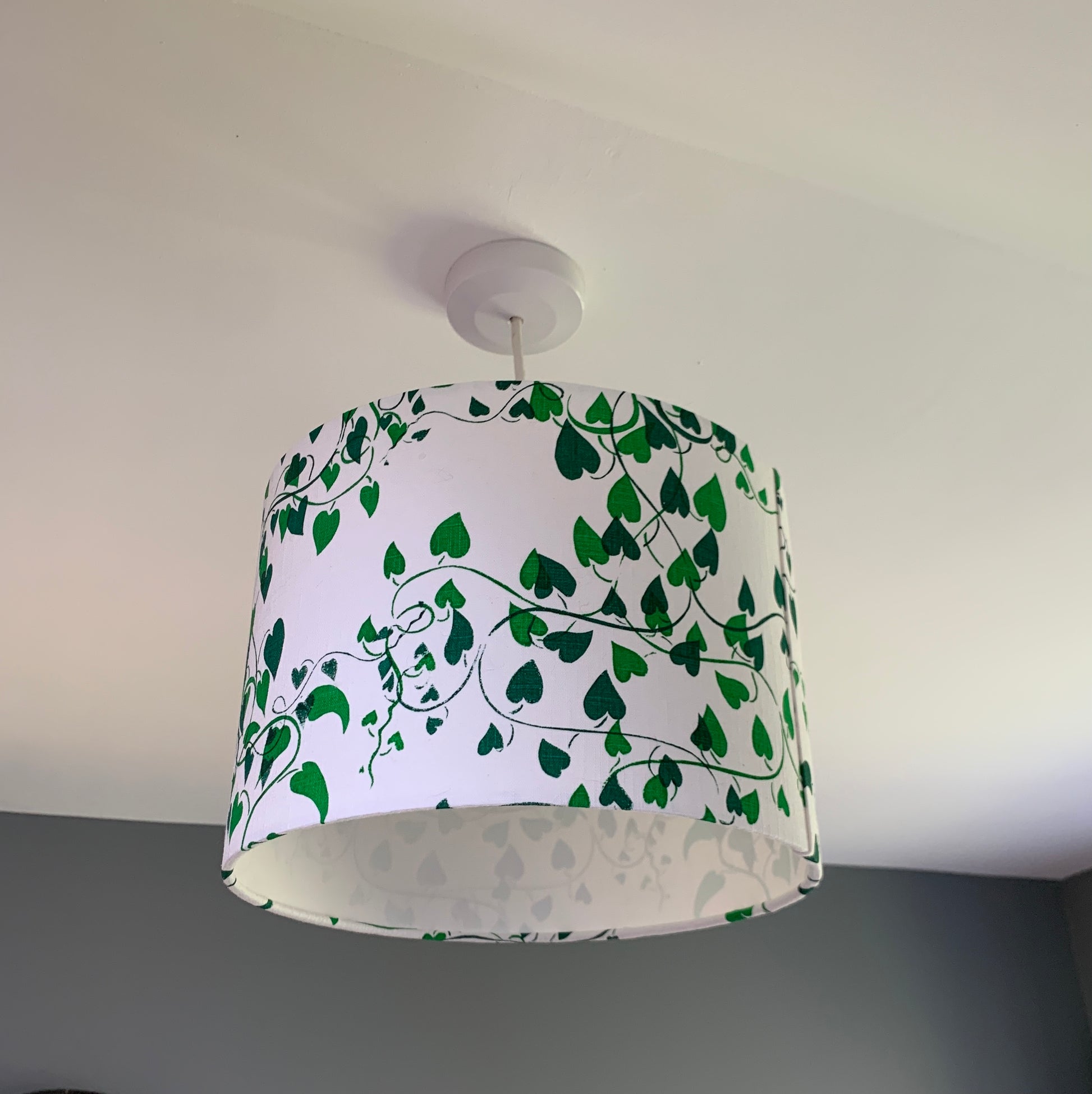 Ceiling hung lampshade with a white linen background and two shades of green convolvulus vines running over it.