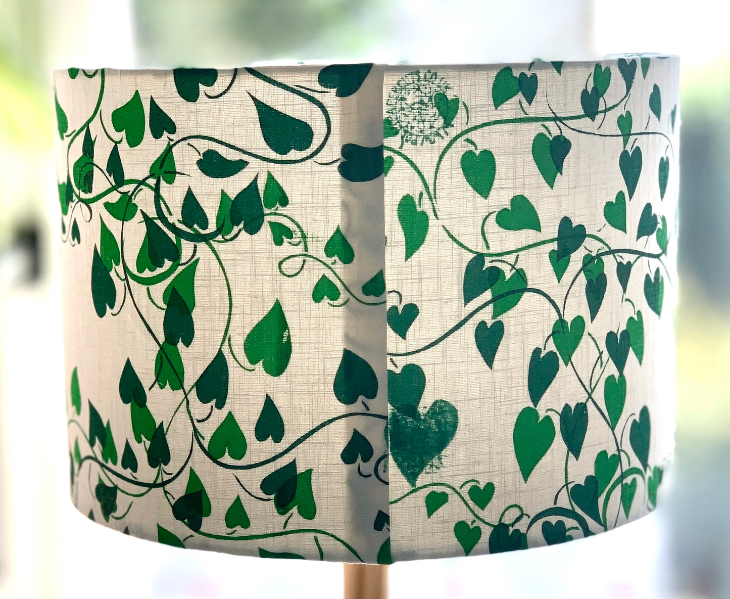 Detail of lampshade with a white linen background and two shades of green convolvulus vines running over it showing seam.