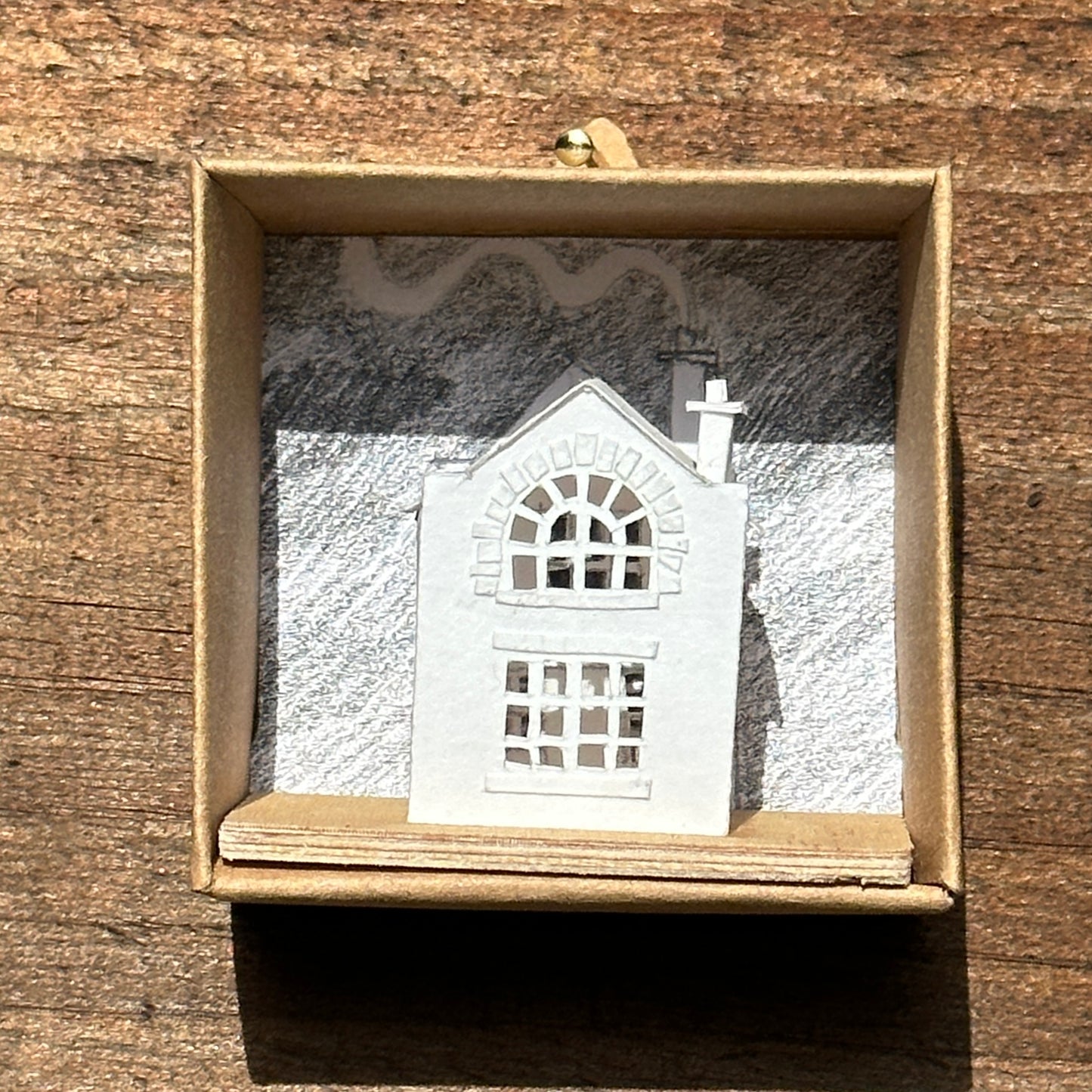 Miniature handmade paper house on plywood base in display box.