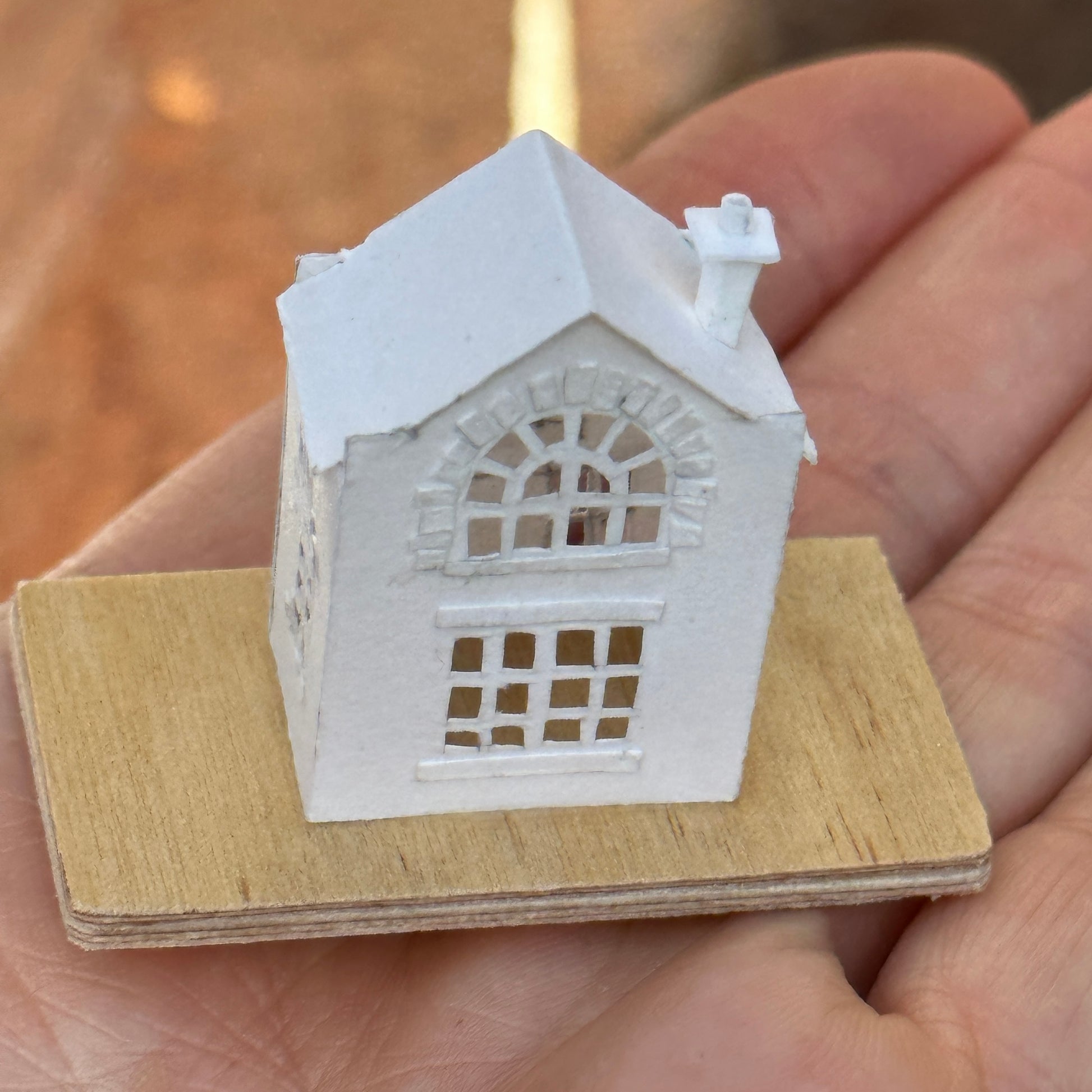 Miniature handmade paper house on plywood base on hand for scale.