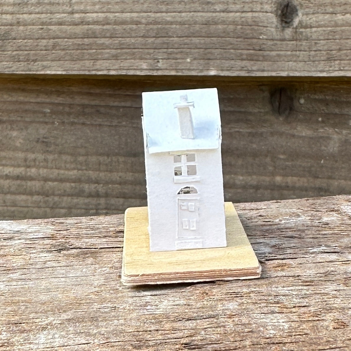 Miniature handmade paper house on plywood base.