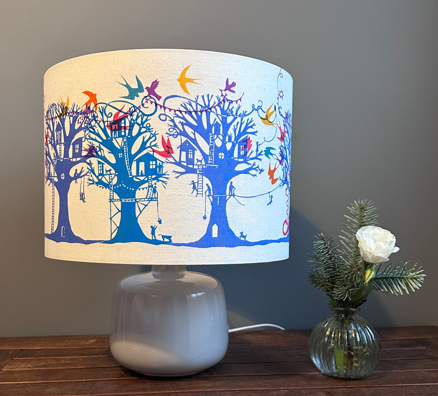 Table lampshade with blue and turquoise  trees with treehouses on cream background with multi coloured birds and bunting.