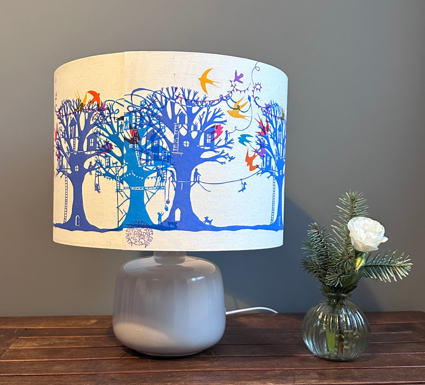 Table lampshade with blue and turquoise  trees with treehouses on cream background with multi coloured birds and bunting.