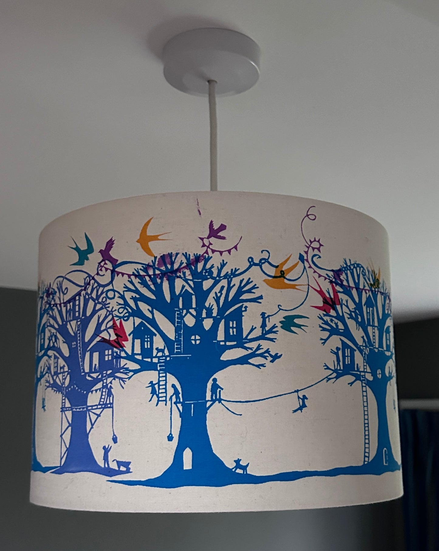 Ceiling lampshade with blue and turquoise  trees with treehouses on cream background with multi coloured birds and bunting.