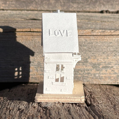 White paper gable fronted house with 'LOVE' applied to roof 