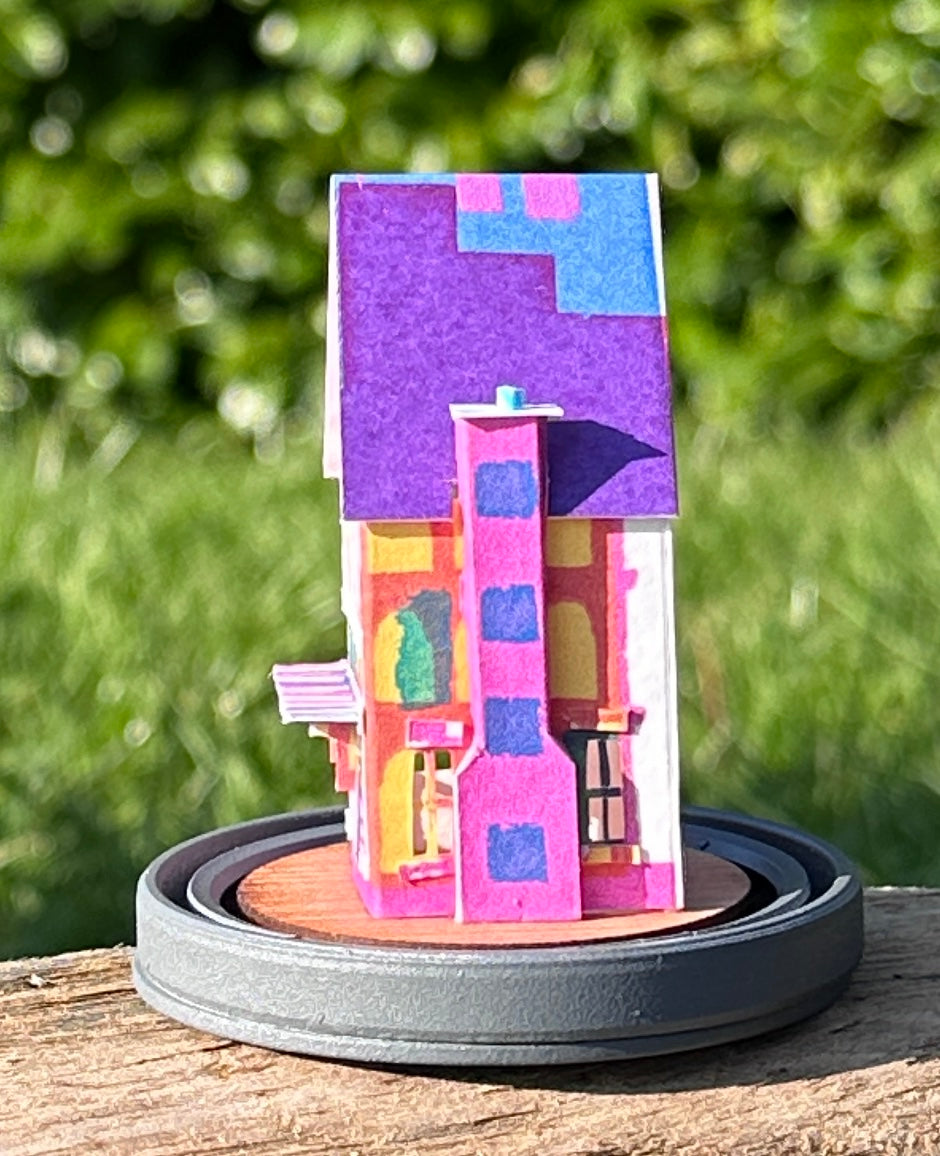 Side elevation of gable roofed house made from multicoloured paper on great wood base