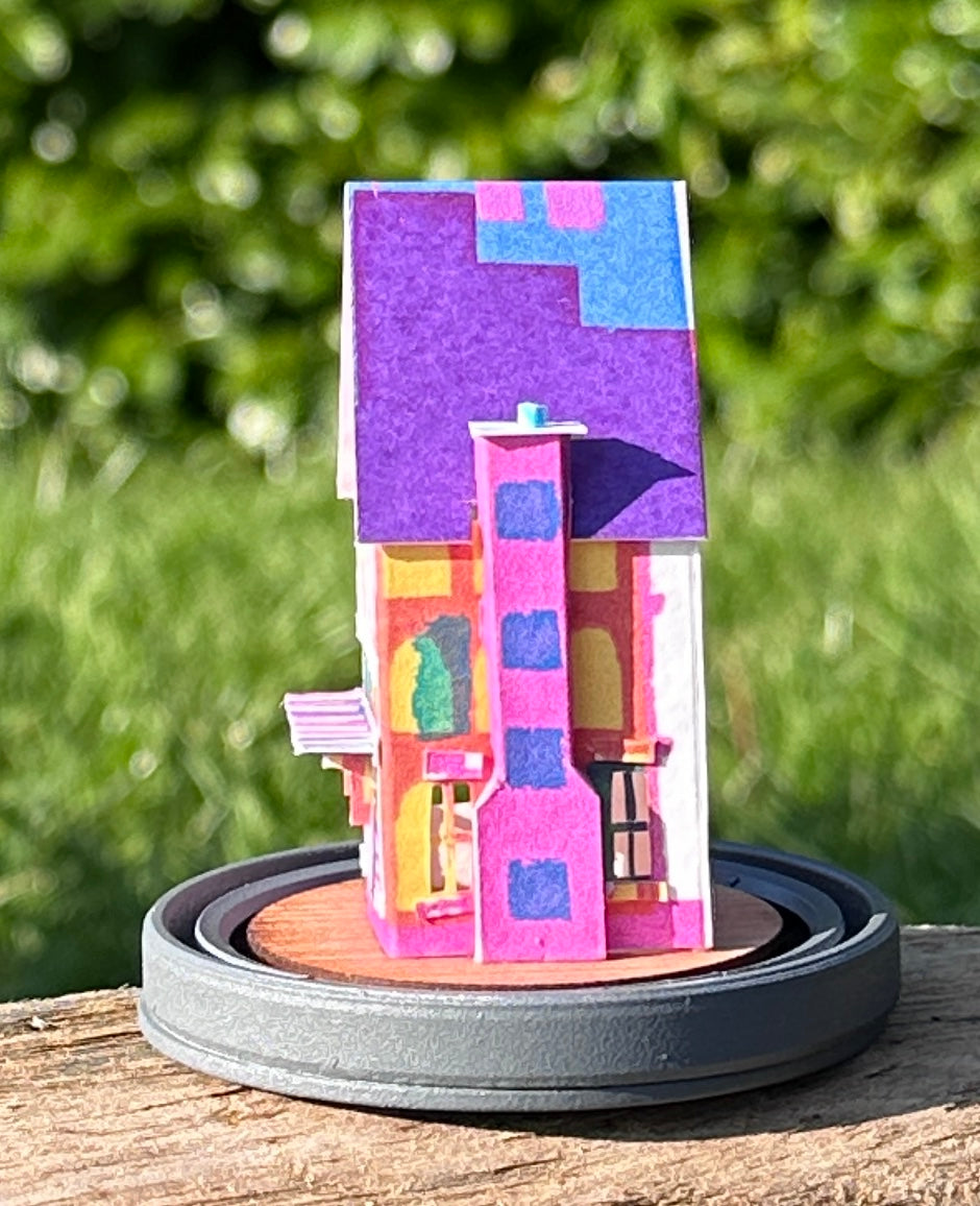 Side elevation of gable roofed house made from multicoloured paper  on great wood base