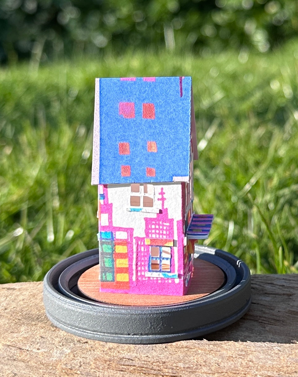 Side elevation of gable roofed house made from multicoloured paper  on grey wood base