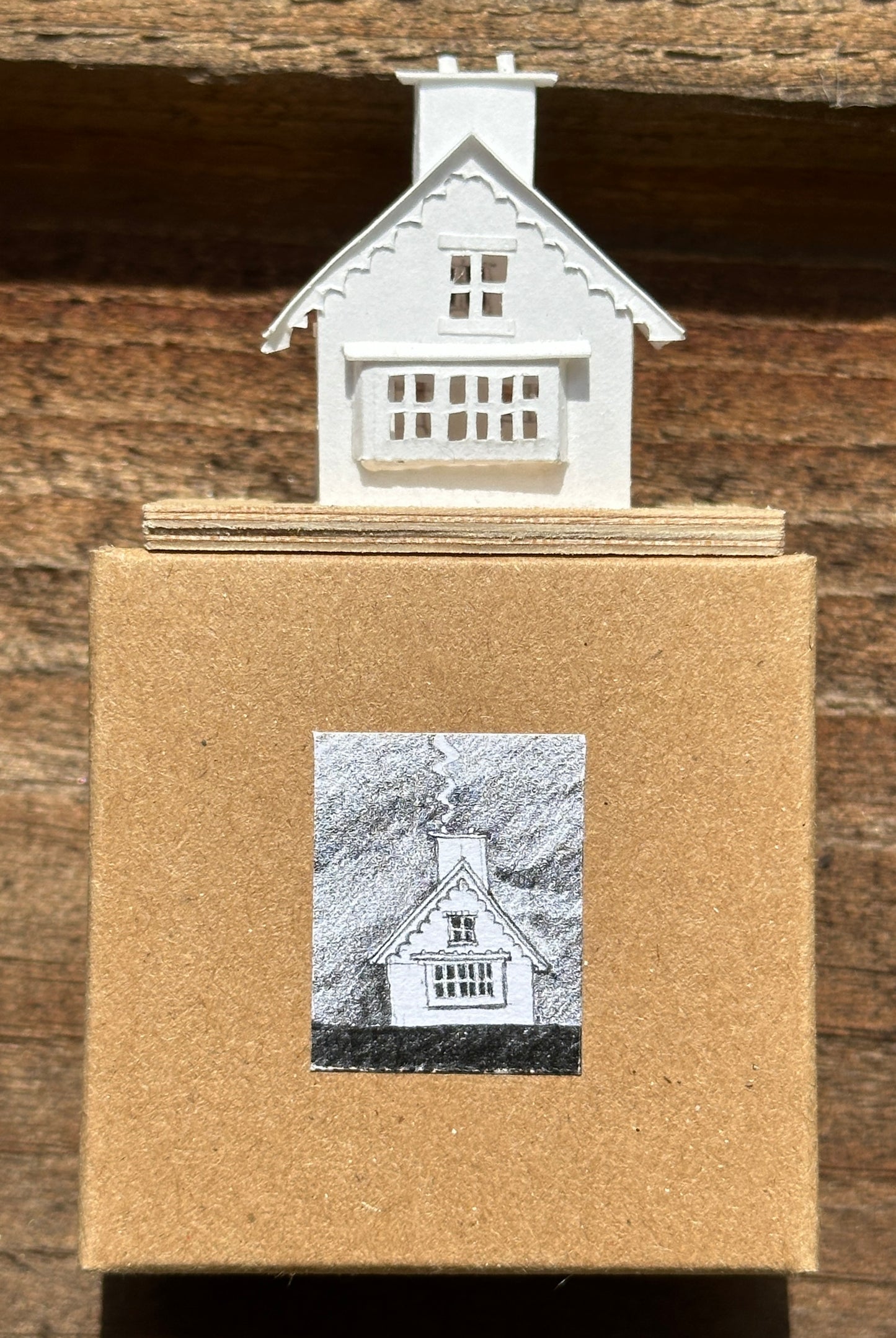 white paper gable fronted house with double chimney on plywood base above presentation box