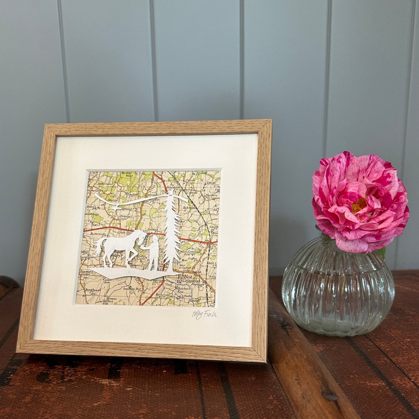 Papercut of horse and girl overlaid and OS Map extract shon in frame next to flower for scale