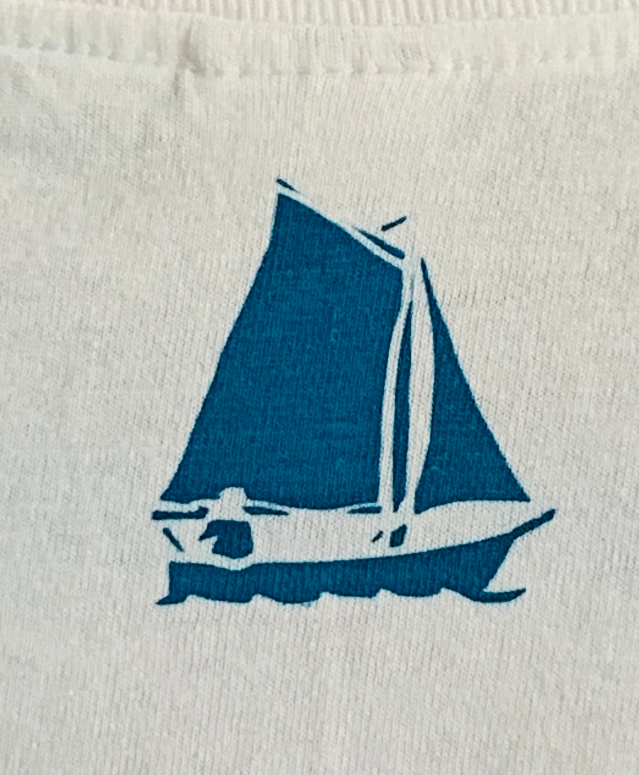 Detail of  turquoise blue boat design  on back of white t-shirt