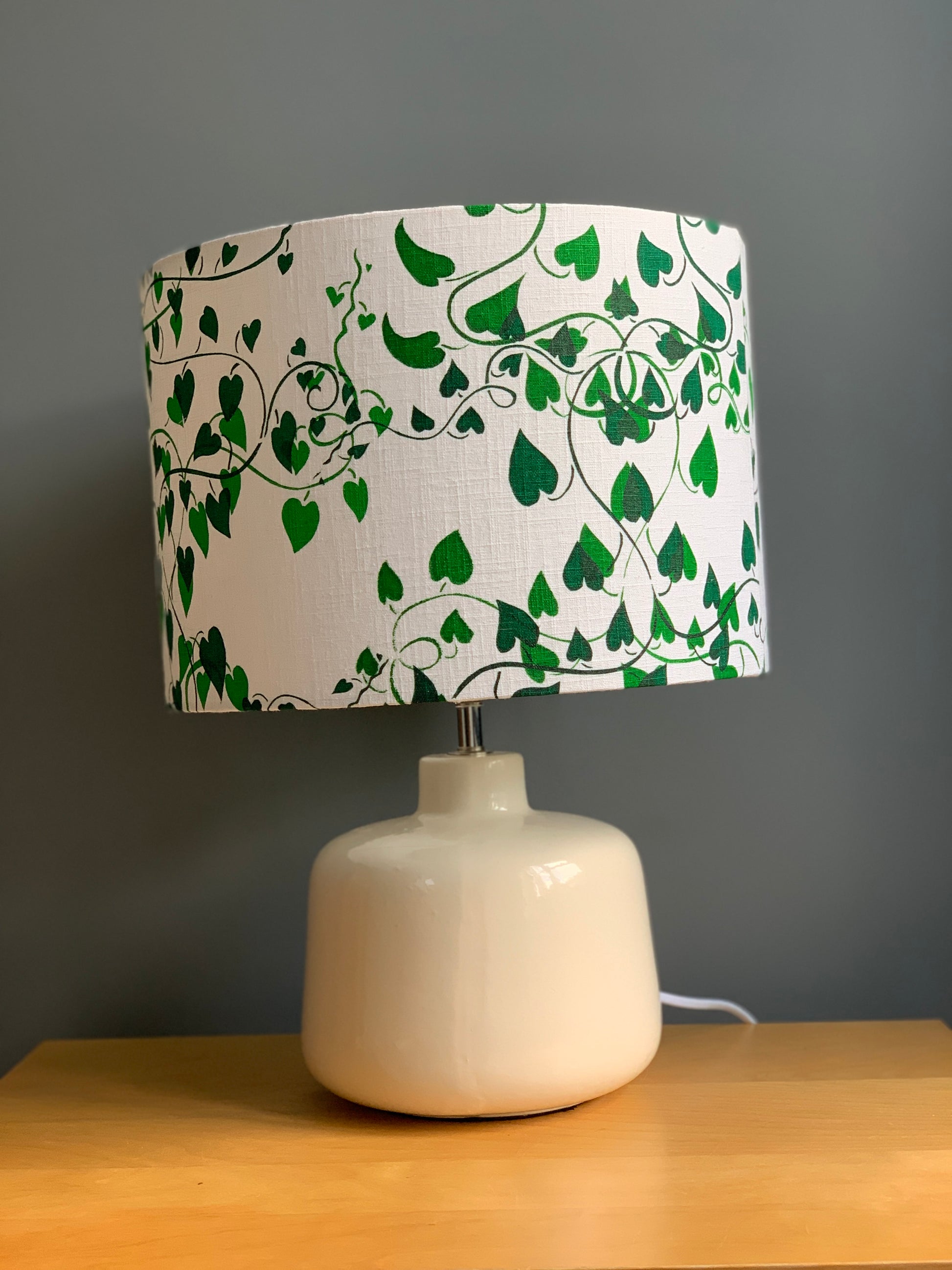 Shades of green on white fabric  handprinted lampshade in  a convolvulus design on cream lamp base.