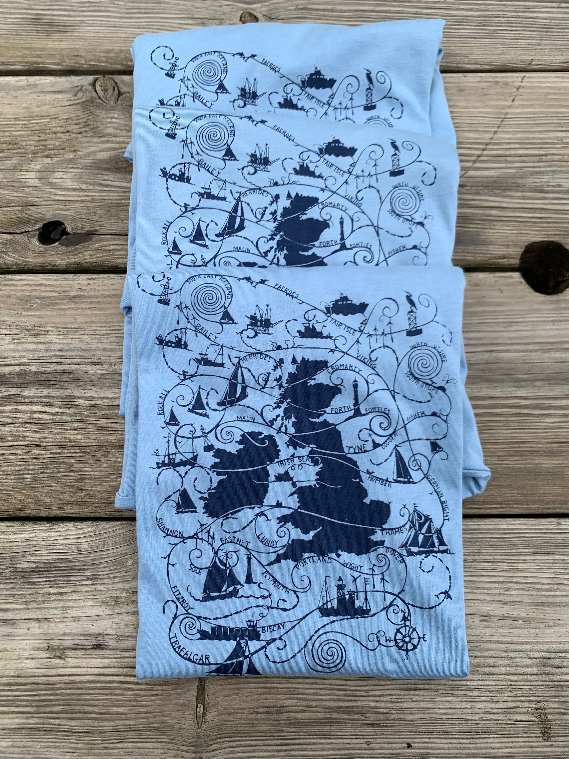 Folded pale blue T-shirts with turquoise blue design  UK map and shipping forecast names