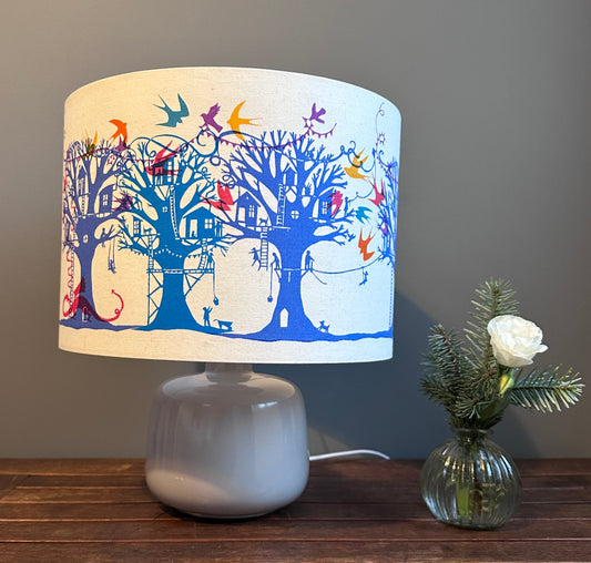 Table lampshade with blue and turquoise  trees with treehouses on cream background with multi coloured birds and bunting.