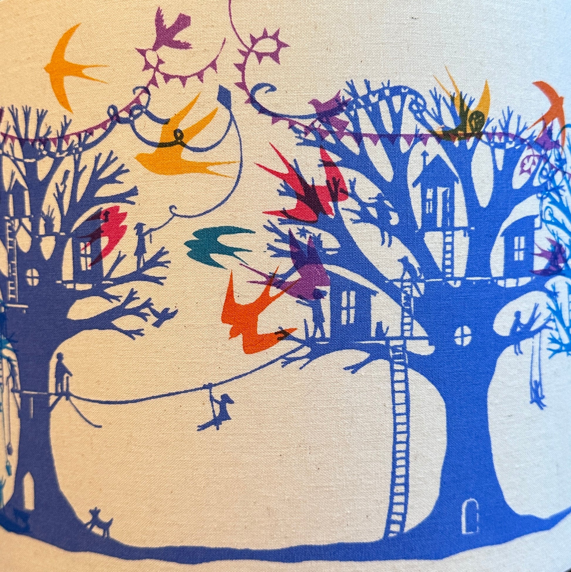 Detail of  lampshade with blue and turquoise  trees with treehouses on cream background with multi coloured birds and bunting.