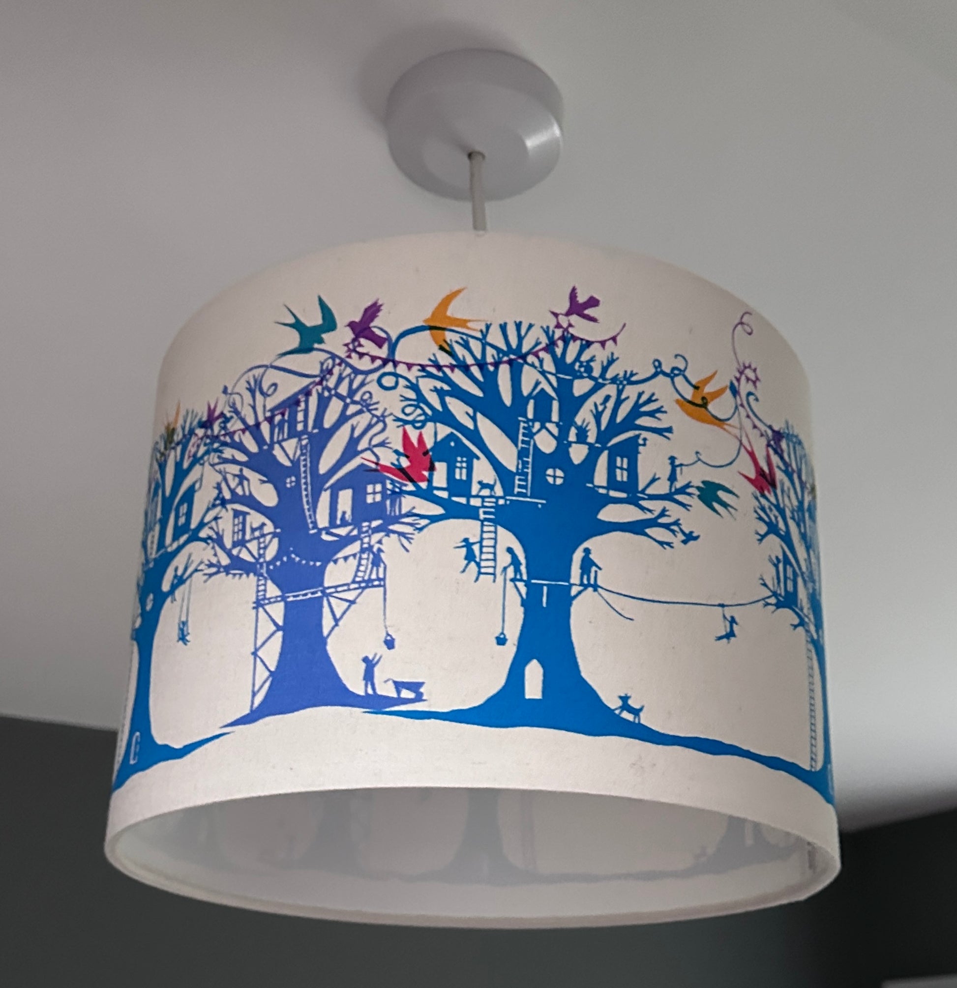 Ceiling lampshade with blue and turquoise  trees with treehouses on cream background with multi coloured birds and bunting.