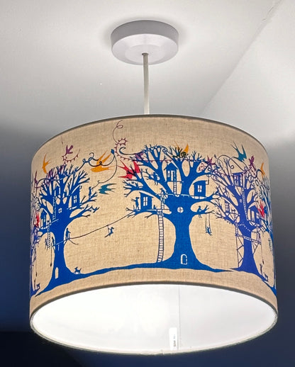 Ceiling lampshade (lit) with blue and turquoise  trees with treehouses on cream background with multi coloured birds and bunting.