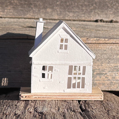 White paper gable fronted house with a heart shaped window and two applied hearts and a  tall chimney