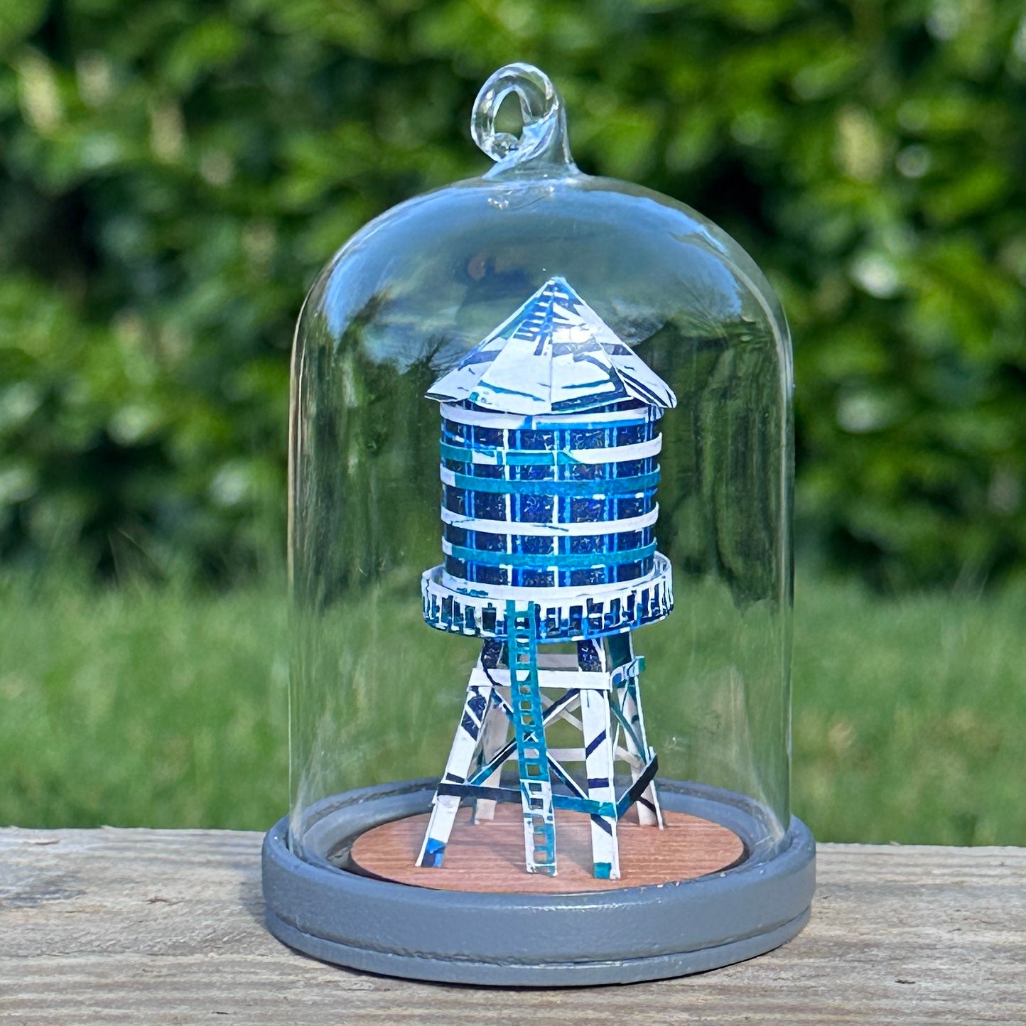 Handcut paper water tower over printed in shades of blue on grey base under glass dome