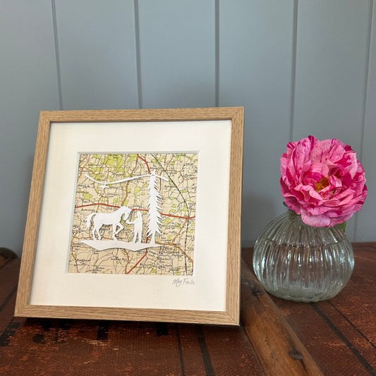Papercut of horse and girl overlaid and OS Map extract shon in frame next to flower for scale