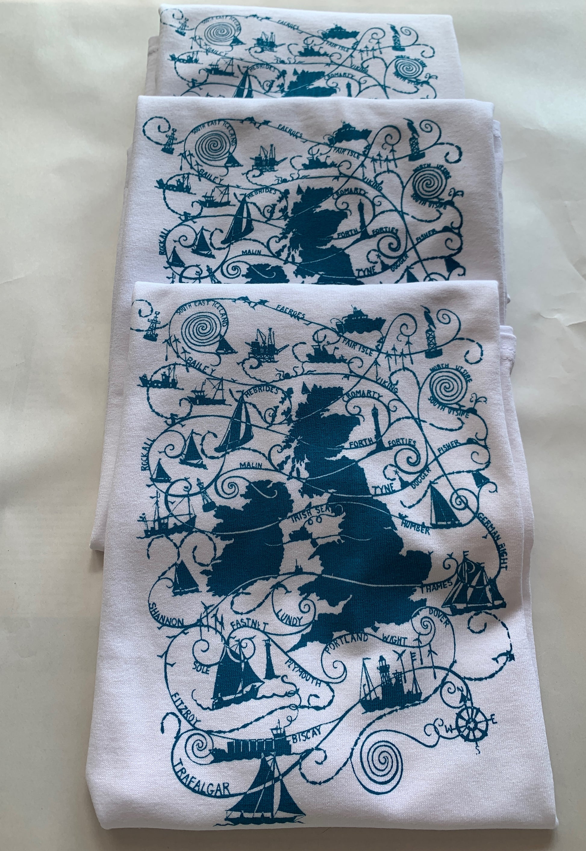 Folded white T-shirts with turquoise blue design  UK map and shipping forecast names